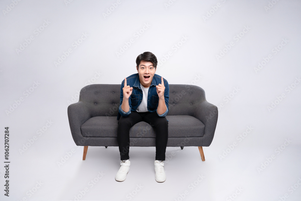 Full body image of young Asian man posing on sofa on white background Full body image of young Asian man posing on sofa on white background