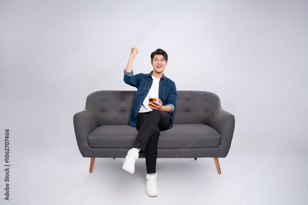 Full body image of young Asian man using phone sitting on sofa on white background Full body image of young Asian man using phone sitting on sofa on white background