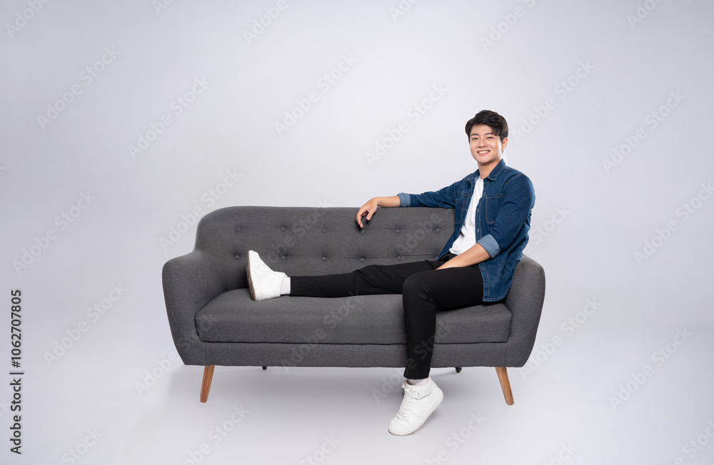 Full body image of young Asian man posing on sofa on white background Full body image of young Asian man posing on sofa on white background