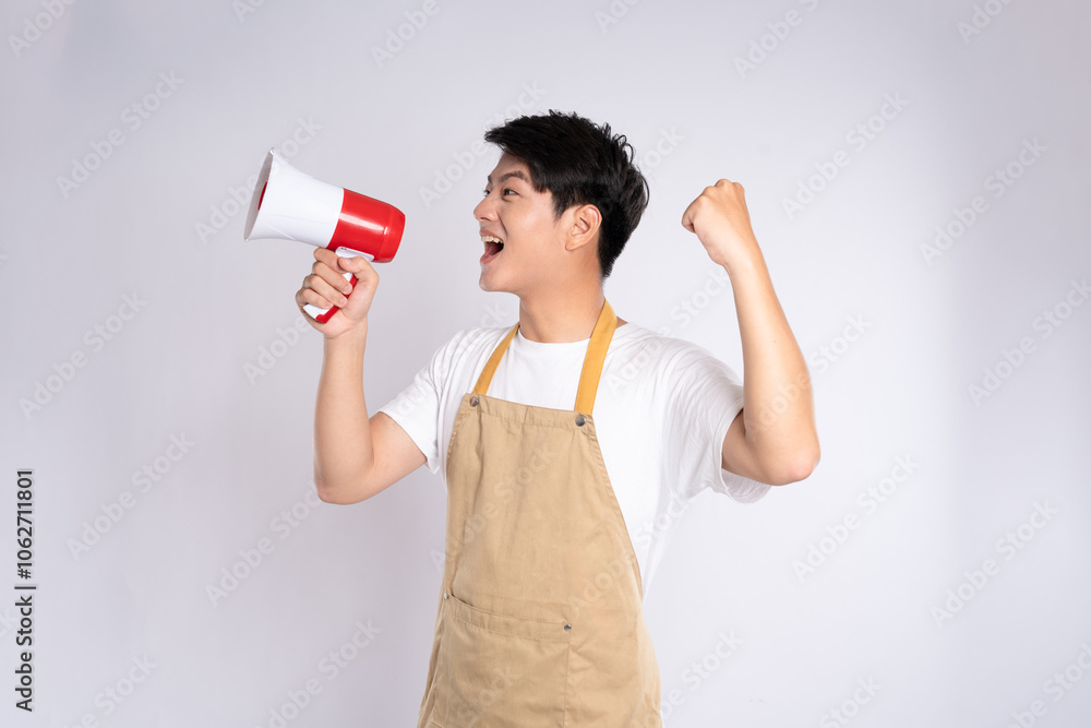 Portrait of young asian man wearing apron holding handspeaker and posing on white background Portrait of young asian man wearing apron holding handspeaker and posing on white background