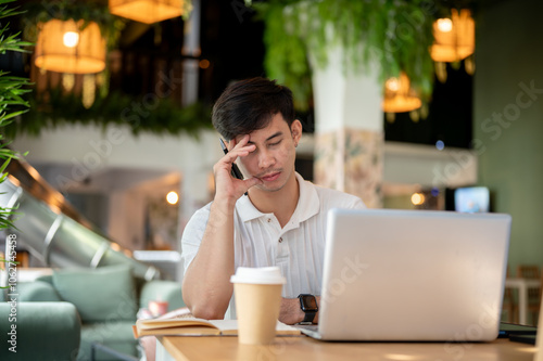 An Asian man working remotely at a coffee shop appears serious, resting his eyes from his computer.