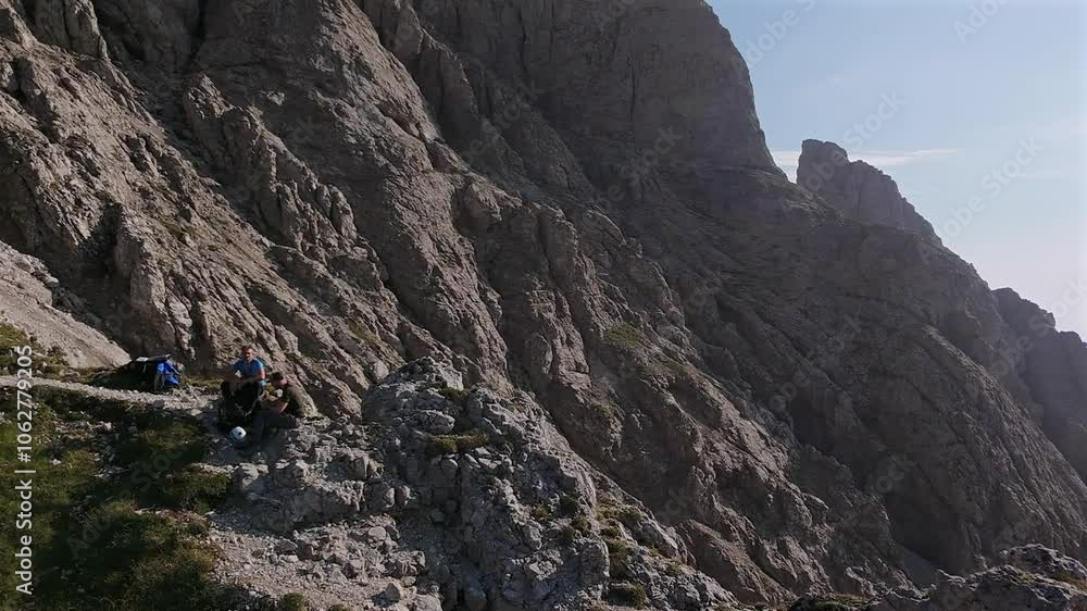 Aerial orbit of two male hikers sitting on top of rugged mountain peak, Italian alps Aerial orbit of two male hikers sitting on top of rugged mountain peak, Italian alps
