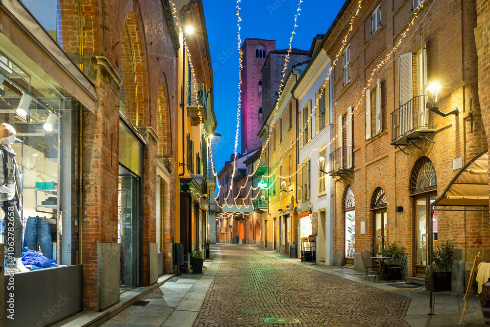 Obraz premium Cobblestone street and old buildings illuminated with Christmas lights in the evening in Alba, Italy.
