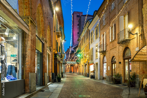 Fototapeta Naklejka Na Ścianę i Meble -  Cobblestone street and old buildings illuminated with Christmas lights in the evening in Alba, Italy.