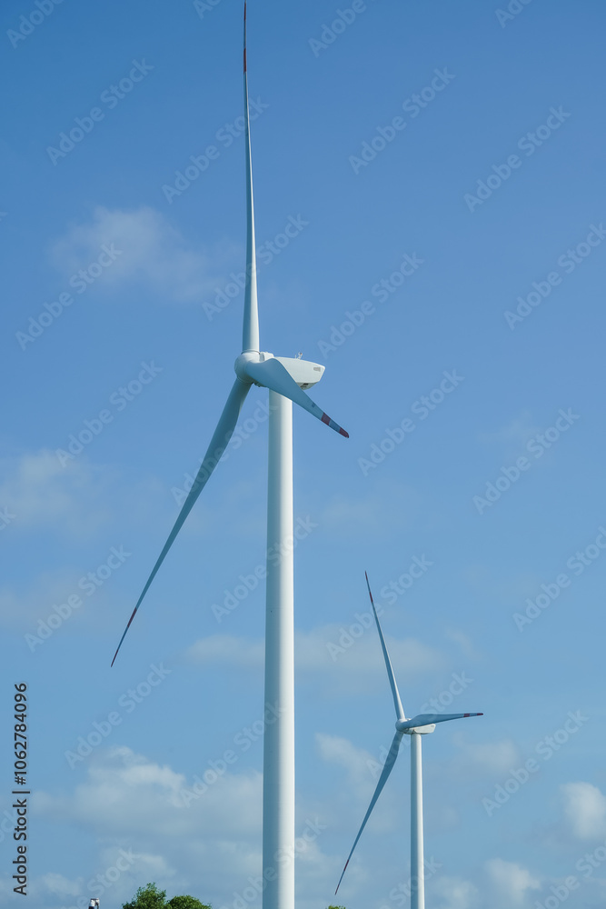 A large wind turbine for generating electricity using the force of the wind installed in an agricultural field against a blue sky. A large wind turbine for generating electricity using the force of the wind installed in an agricultural field against a blue sky.