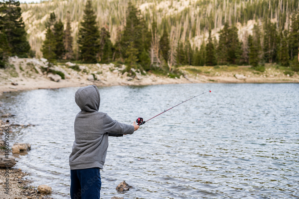 Person casting fishing line by lakeside wearing hoodie Person casting fishing line by lakeside wearing hoodie