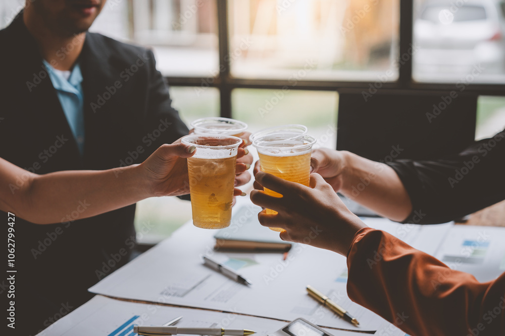 Team of business men and women sitting at desks with documents, graphs, charts, holding glasses of champagne, clinking beers, celebrating a party in business success together in the office. Team of business men and women sitting at desks with documents, graphs, charts, holding glasses of champagne, clinking beers, celebrating a party in business success together in the office.