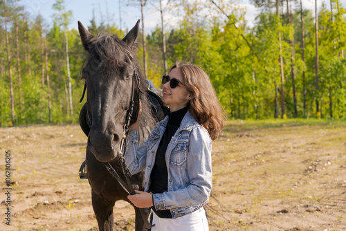 Woman is standing next to a black horse