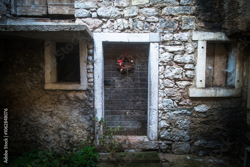 Dettaglio della facciata di una casa abbandonata del borgo di Erto nei pressi della diga del Vajont con finestre chiuse e sulla porta una ghirlanda natalizia photo