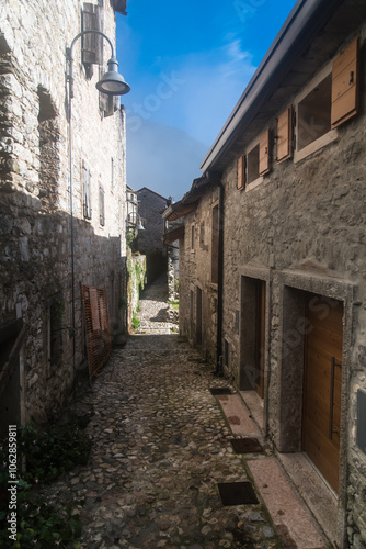 Un vicolo del borgo di Erto presso la diga del Vajont con la sua pavimentazione ad acciottolato passa fra alcune case in una giornata di sole photo