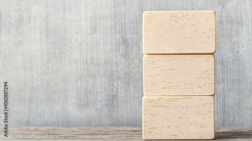 A minimalist stack of three light-colored blocks rests on a wooden surface against a textured wall, conveying simplicity and calm.