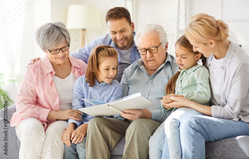 Three generations family portrait enjoying watching childhood picture album hugging beloved senior grandparents, sit close embracing, cuddling grandchildren on couch at home, spending time together photo