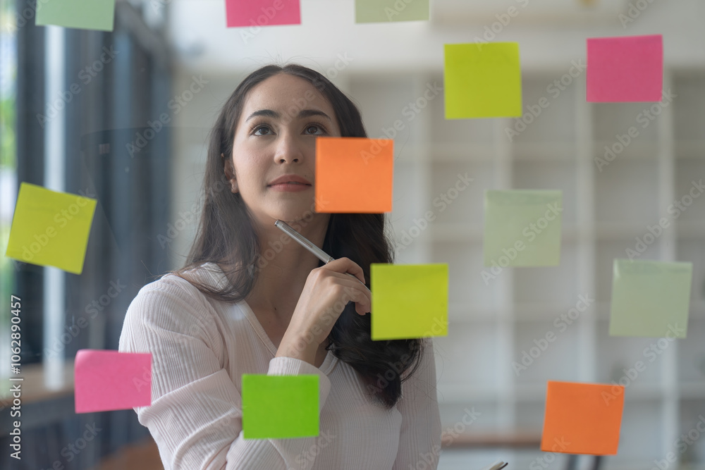 Asian businesswomen use post-it notes on glass walls to write strategic business plans to develop and succeed. Asian businesswomen use post-it notes on glass walls to write strategic business plans to develop and succeed.