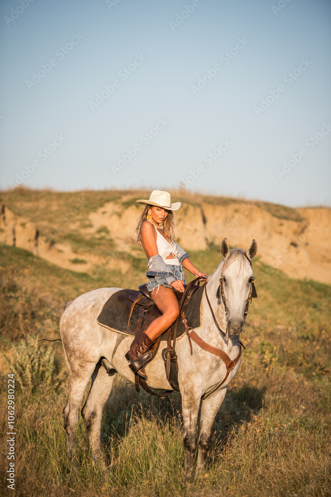 Sexy cowgirl with hat and denim on horseback in the desert. Beautiful girl in a cowboy hat on a horse. Beautiful cowgirl on horseback in the mountains. Outdoor lifestyle portrait