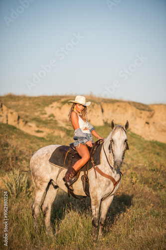 Obraz na płótnie Sexy cowgirl with hat and denim on horseback in the desert. Beautiful girl in a cowboy hat on a horse. Beautiful cowgirl on horseback in the mountains. Outdoor lifestyle portrait w salonie