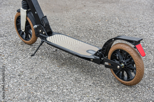 The deck of a folding scooter with beige wheels stands on the asphalt.