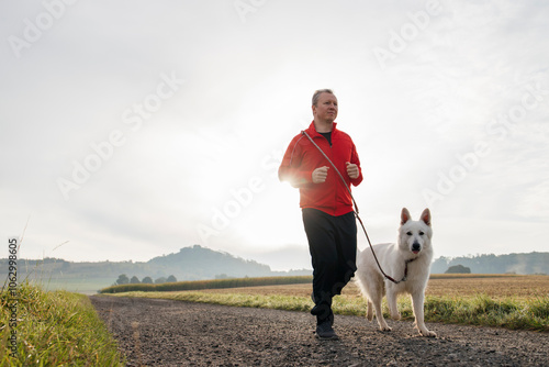 Mid adult man with Swiss shepherd dog jogging on dirt road under sky photo