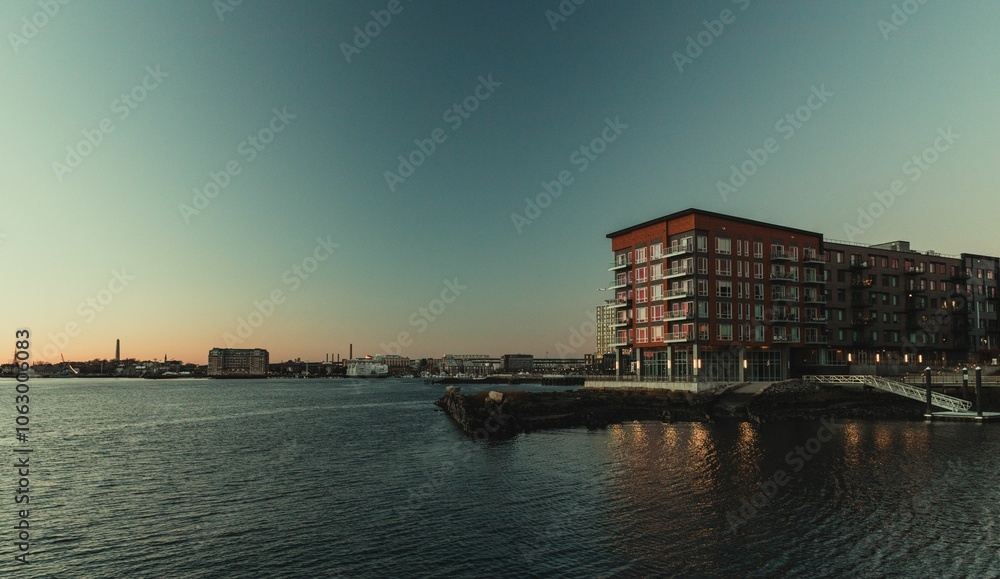 Naklejka premium Sunset over waterfront cityscape with modern apartments.
