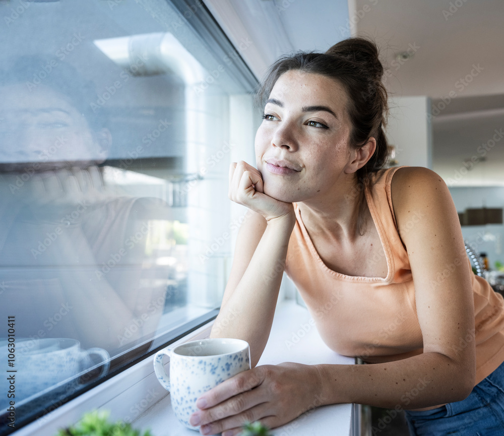 Smiling woman leaning on window sill with coffee cup at home Smiling woman leaning on window sill with coffee cup at home