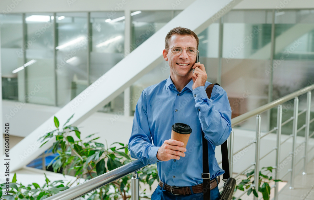 Smiling businessman talking on smart phone near railing in office Smiling businessman talking on smart phone near railing in office