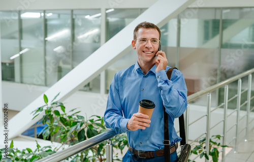 Smiling businessman talking on smart phone near railing in office photo