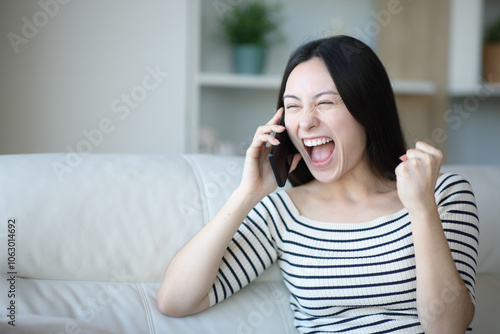 Excited asian woman talking on phone at home