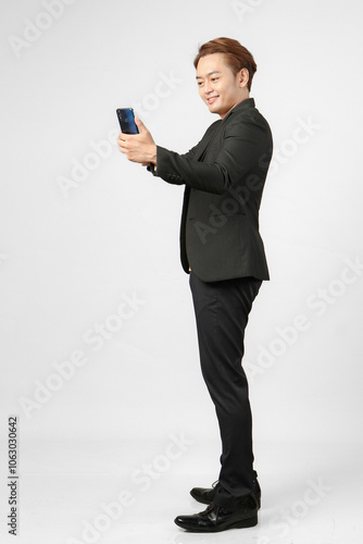 full length shoot of cheerful happy asian business man wearing suit holding mobile phone on isolated background.