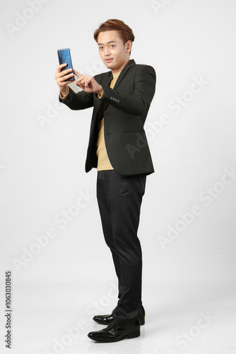 full length shoot of cheerful happy asian business man wearing suit holding mobile phone on isolated background.