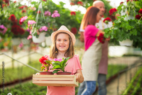 Little girl holding flowers in a greenhouse with family photo