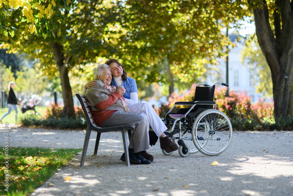 Elderly woman enjoying cup of coffee with her nurse in the park during warm autumn day. Young caregiver spending time with senior woman. Elderly woman enjoying cup of coffee with her nurse in the park during warm autumn day. Young caregiver spending time with senior woman.