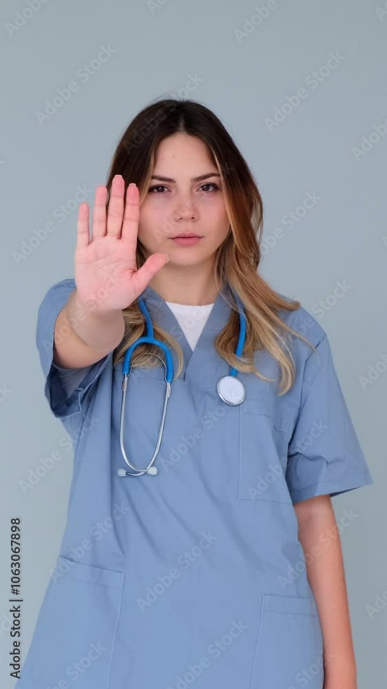Portrait of a Caucasian young adult female doctor or nurse showing stop sign in denial and opposition on blue background. Vertical video. Portrait of a Caucasian young adult female doctor or nurse showing stop sign in denial and opposition on blue background. Vertical video.
