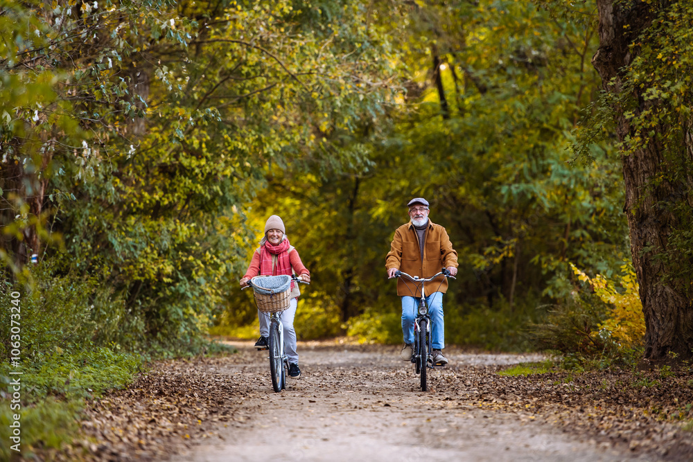 Fototapeta premium Beautiful elderly couple on bike ride in the forest. Seniors in love cycling through autumn nature, enjoying a peaceful moment.