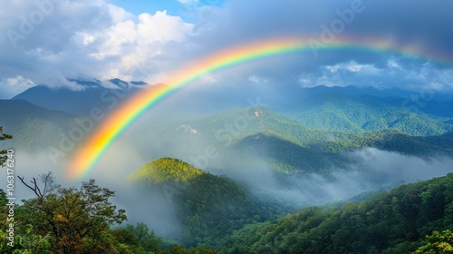 A rainbow stretches over misty mountains with soft clouds rolling over the ridges