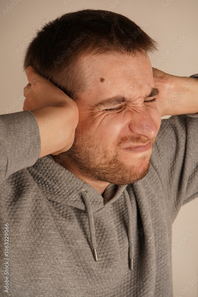 Portrait of young guy closing his ears by hands and keeping his eyes closed while isolated on grey. Photo of desperate annoyed bearded man keeps hands on head and closes eyes. Man in depression.` Portrait of young guy closing his ears by hands and keeping his eyes closed while isolated on grey. Photo of desperate annoyed bearded man keeps hands on head and closes eyes. Man in depression.`