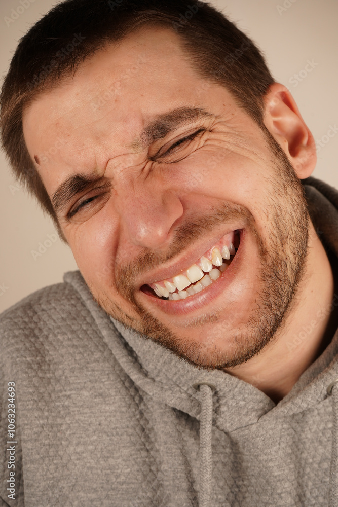 Obraz premium Cheerful, happy enthusiastic man laughing. Grinning joyfully, Portrait of pleased positive male laughs joyfully, expresses happiness, stands against grey background. Happy amazed satisfied young man.