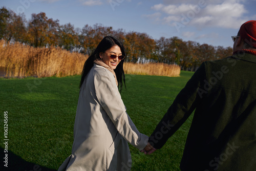 A loving couple walks hand in hand through a park, enjoying a sunny autumn day together. photo