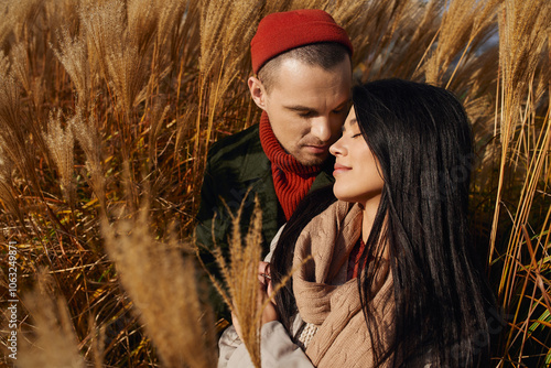 A couple wrapped in warm attire share a tender moment in a field of autumn grass. photo