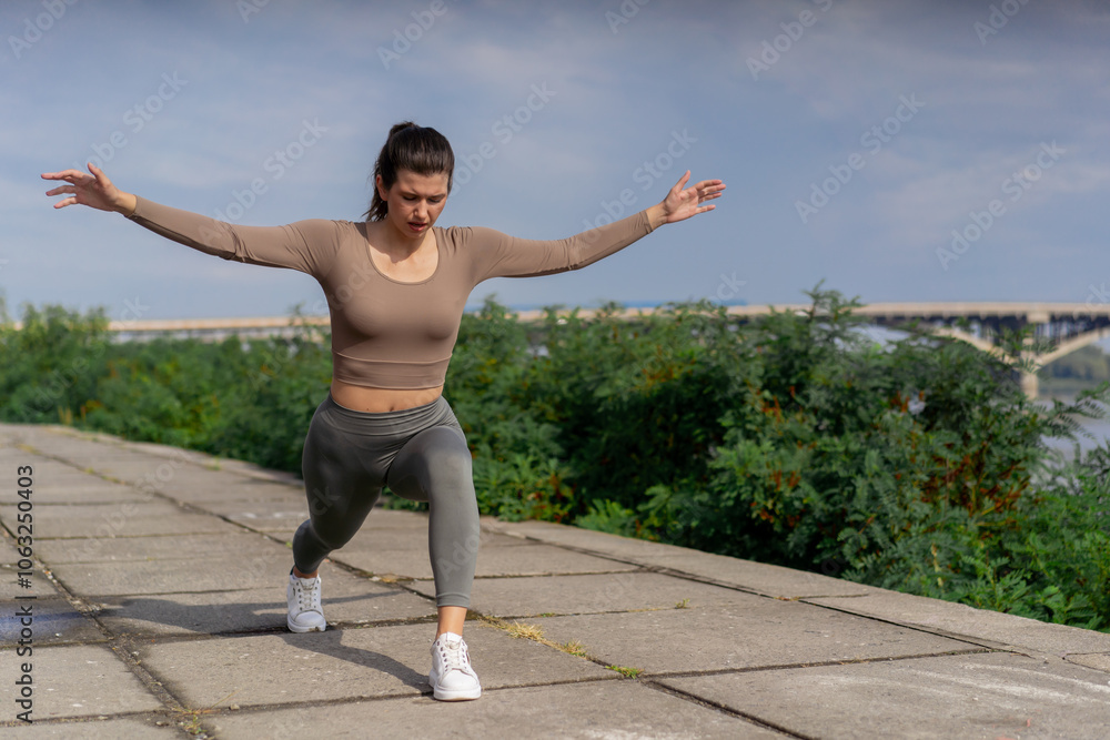 on the street on the river embankment in the city center on a concrete path a sporty girl in gray sports suit healthy lifestyle warm-up imperfect figure on the street on the river embankment in the city center on a concrete path a sporty girl in gray sports suit healthy lifestyle warm-up imperfect figure