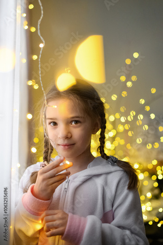 Girl Looking Out the Window with Festive Garland Lights in Background