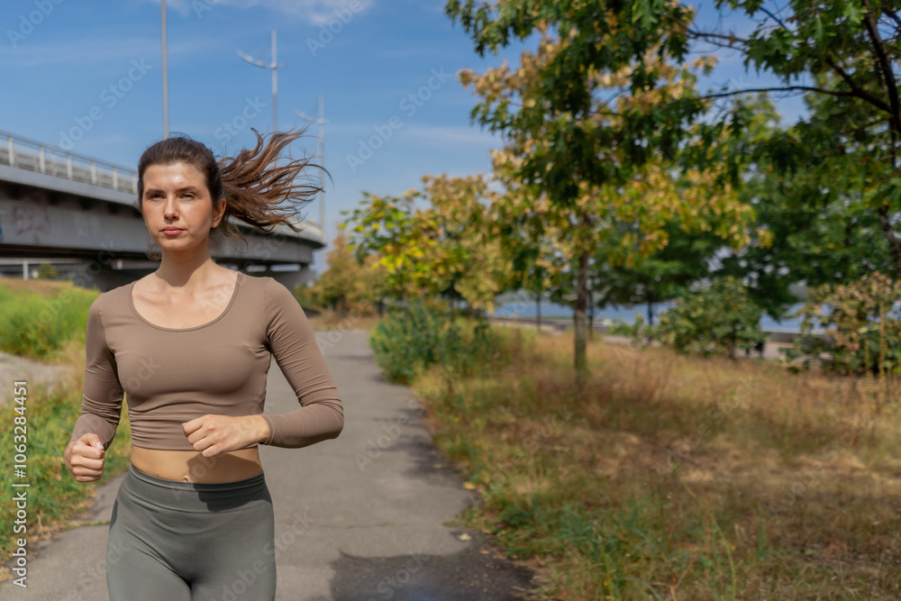 Fototapeta premium on the street on the river embankment in the city center on concrete path a sporty girl in a gray sports suit healthy lifestyle morning jogging imperfect figure