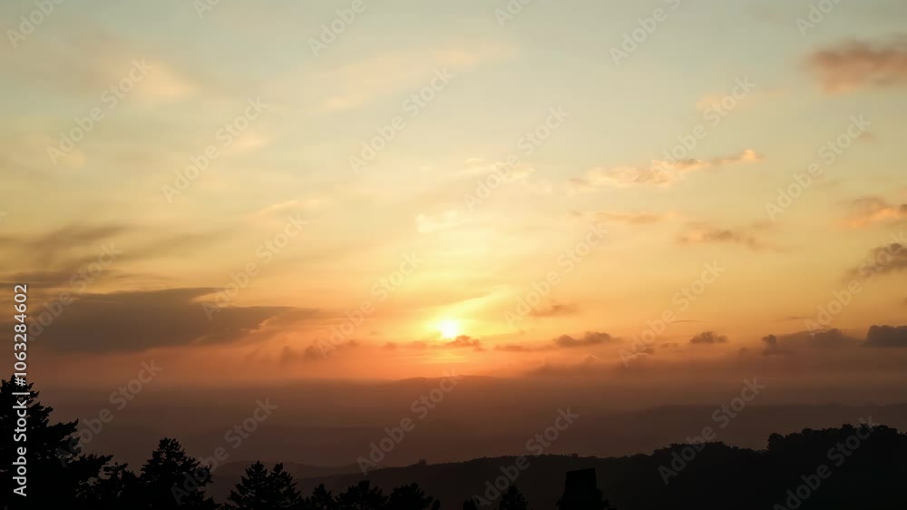 Golden sunset over a hazy mountain range with silhouetted trees in the foreground. Golden sunset over a hazy mountain range with silhouetted trees in the foreground.