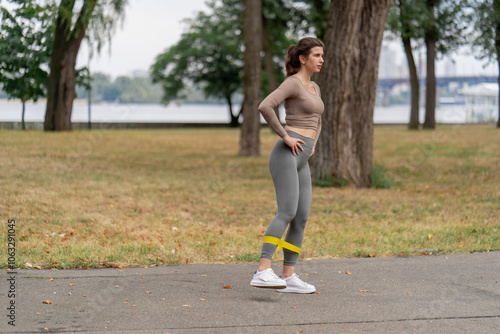 on the street in the park in the city center two girls in dark sportswear pumping up their legs and butt with yellow fitness band