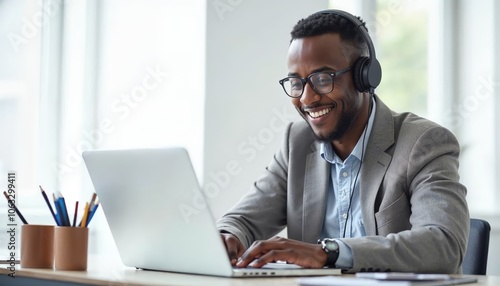 Young African American Man Smiling While Working on a Computer with Headset in Modern Office Environment