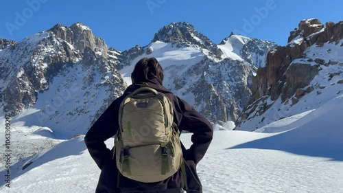 Skiers climbing a snowy slope in the mountains of Almaty, Kazakhstan, with majestic peaks in the background under a bright blue sky. A scene of winter adventure and alpine exploration.