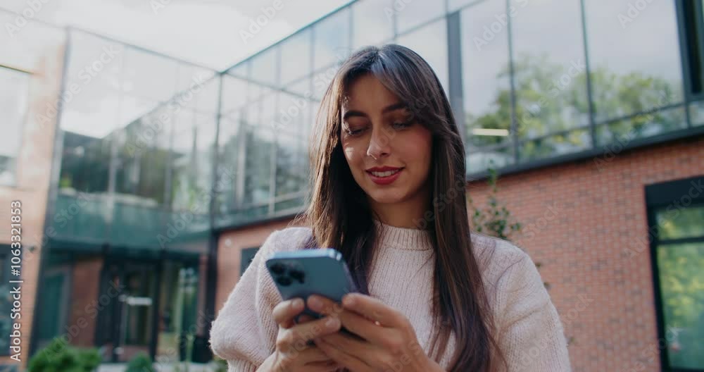 Charming Caucasian woman using her smartphone with both hands. Entering message or text on smartphone with her fingers. Remote communication concept. Browsing social media in fresh air. Charming Caucasian woman using her smartphone with both hands. Entering message or text on smartphone with her fingers. Remote communication concept. Browsing social media in fresh air.
