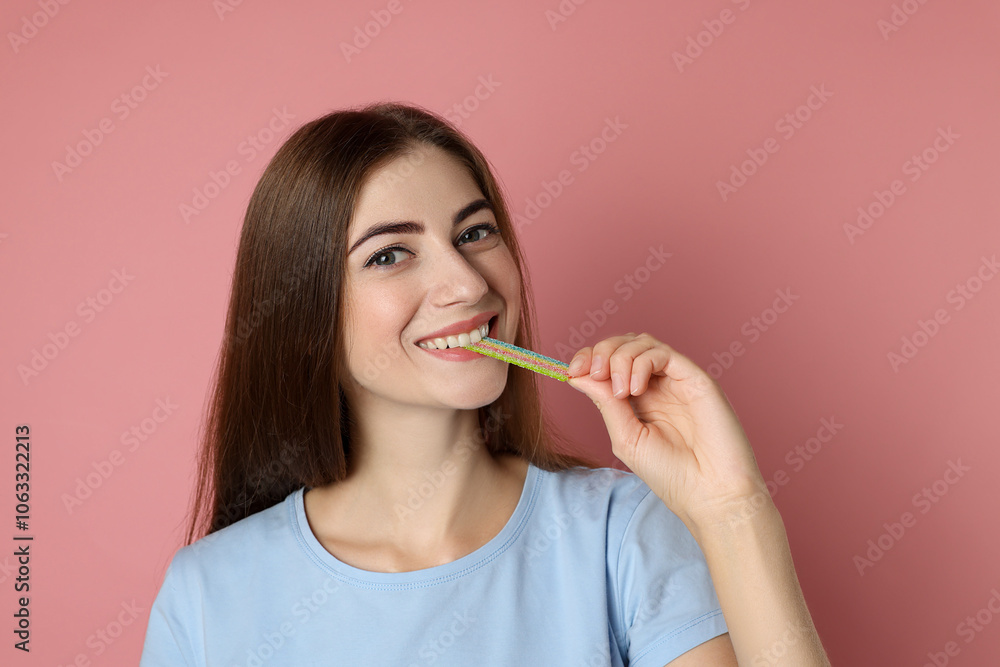 Young woman eating tasty rainbow sour belt on pink background Young woman eating tasty rainbow sour belt on pink background