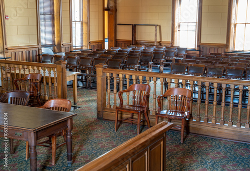 An empty audience section of a courtroom with ornate wooden arm chairs for seating and railing for separation from the trial with leather top table, Presidio County Courthouse, Marfa, Texas
