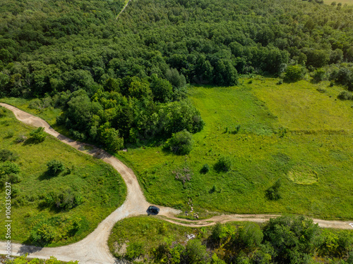 Stunning landscape in Saka, Estonia. Expansive view of the countryside, characterized by lush green fields and dense forests. A single car parked on the dirt road. photo