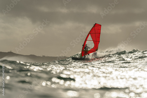 Canvas Print A windsurfer with a bright red sail rides a wave at sea