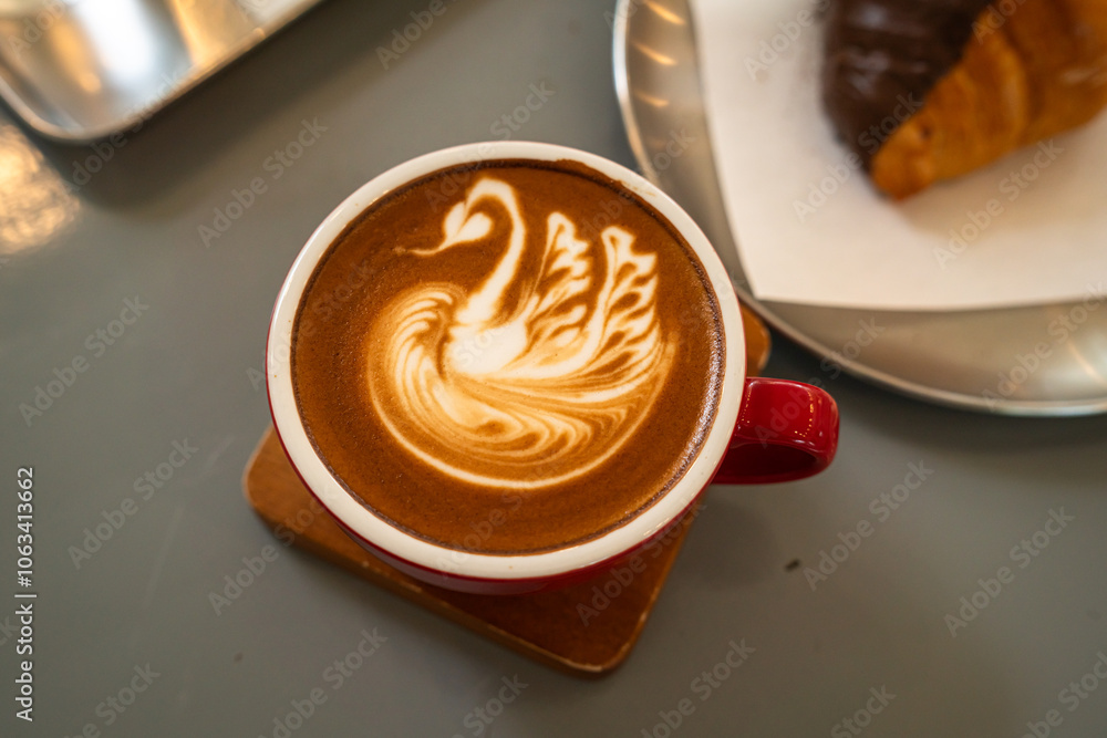 Hot coffee latte with latte art milk foam a swan shape in cup mug with chocolate Croissant on wood desk on top view.As breakfast In a coffee shop at the cafe,during business work concept,Rainy season